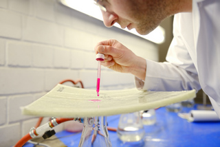 Laborant träufelt pinke Prüfflüssigkeit mit einer Pipette auf eine Materialprobe