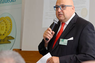 Mann mit blauer Brille und roter Krawatte moderiert mit Mikrofon in der Hand