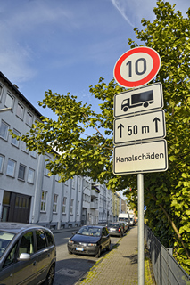 Verkehrsschild mit Tempo 10 für Lkw auf 50 Metern wegen Kanalschäden an einer innerstädtischen Straße.