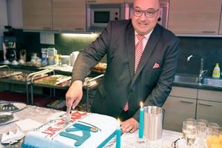 Mann mit Glatze, Brille und Anzug schneidet Torte an